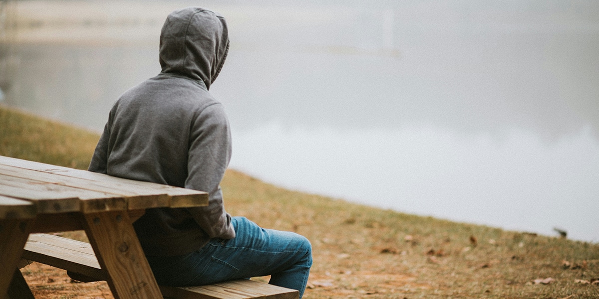 person sitting in silence on a bench by water
