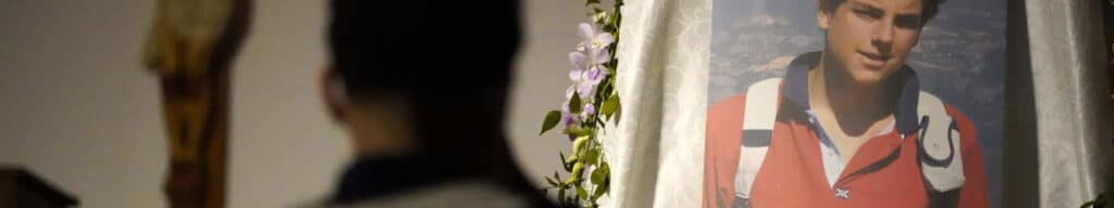 A young man says a prayer in front of a photo of St. Carlo Acutis.