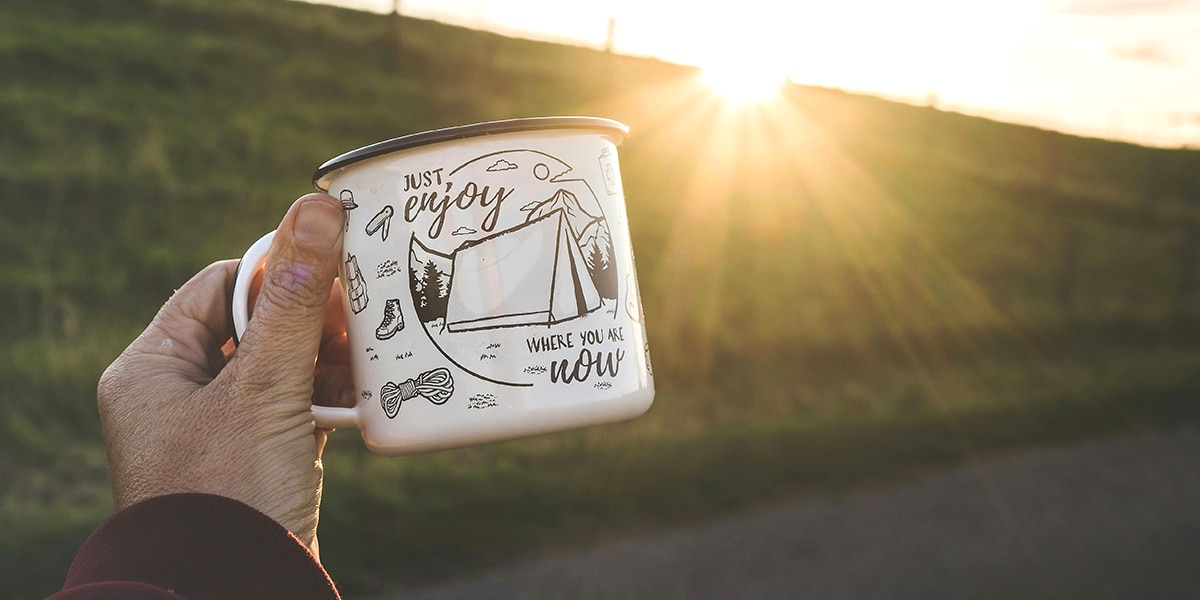 hand holding a mug with the words imprinted "Just enjoy where you are now"