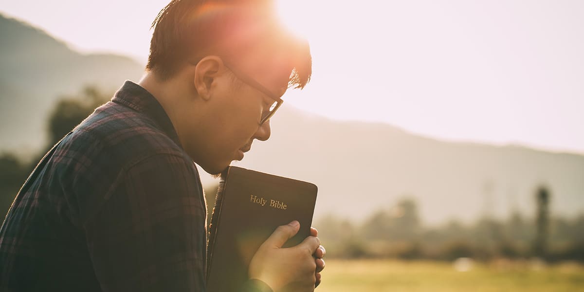 Man praying while holding a Bible.