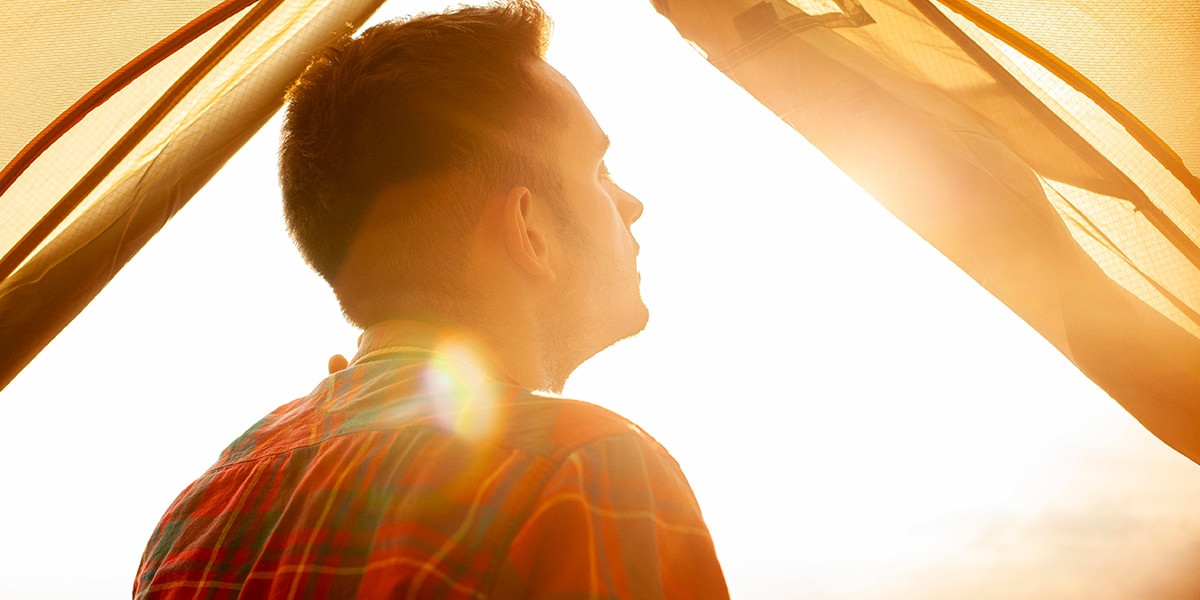 man in a tent reflecting while surrounded by warm light.