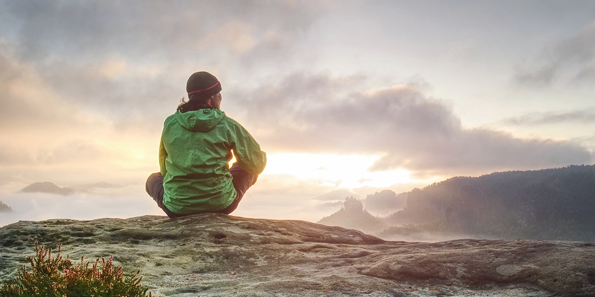 man sitting peacefully watching a sunrise in the mountains