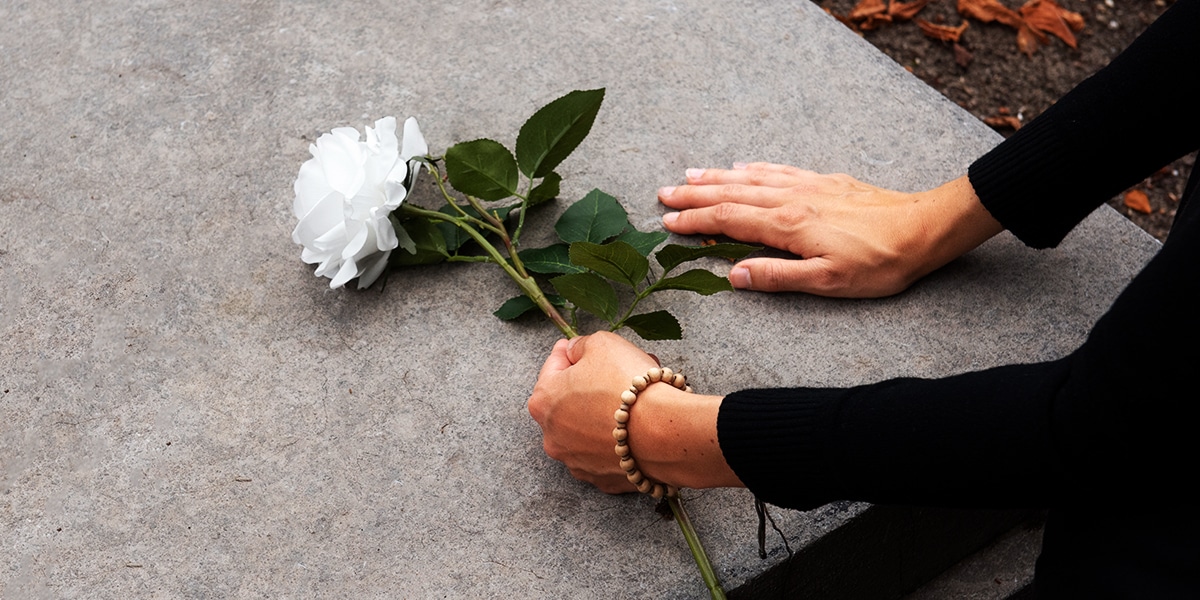 Mother putting her hands on a grave while holding a white flower.