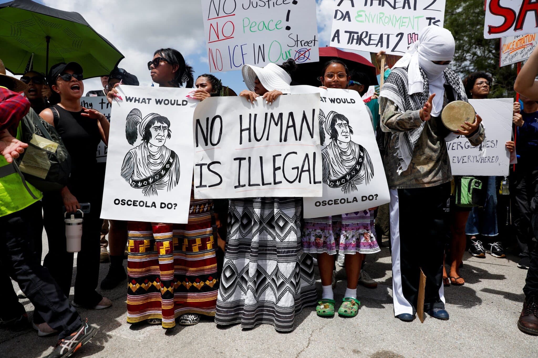 Protesters flank an entrance road at a temporary migrant detention center nicknamed "Alligator Alcatraz" in Ochopee, Fla.