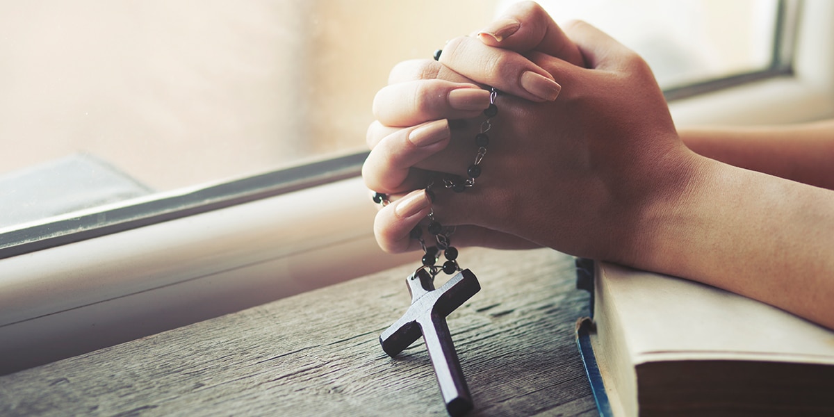 folded hands holding a rosary with a cross, praying
