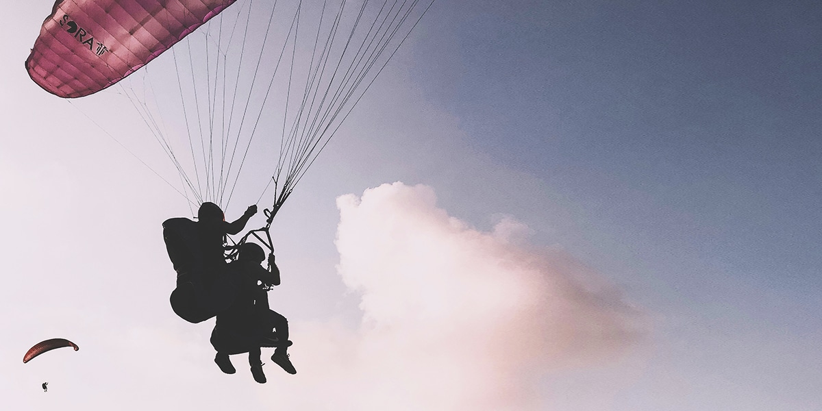 couple are flying through the air on one parachute