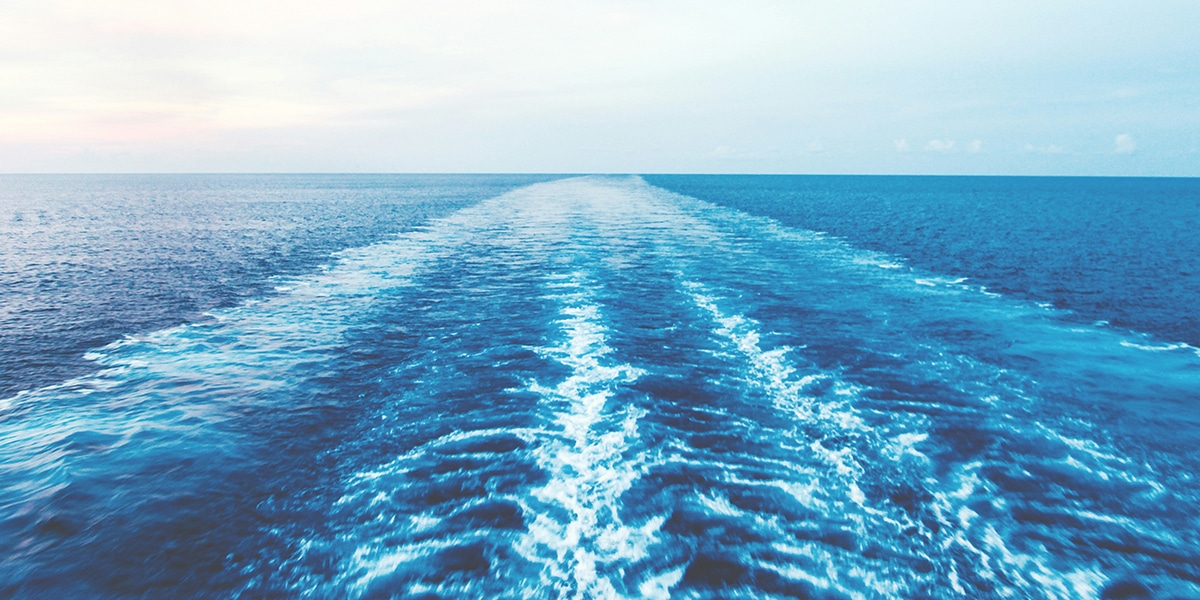 boat traveling through the blue water ocean leaving behind a wake and waves