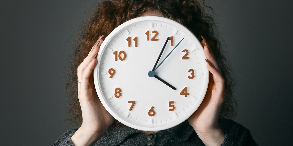woman holding a clock in front of her face, showing the time.
