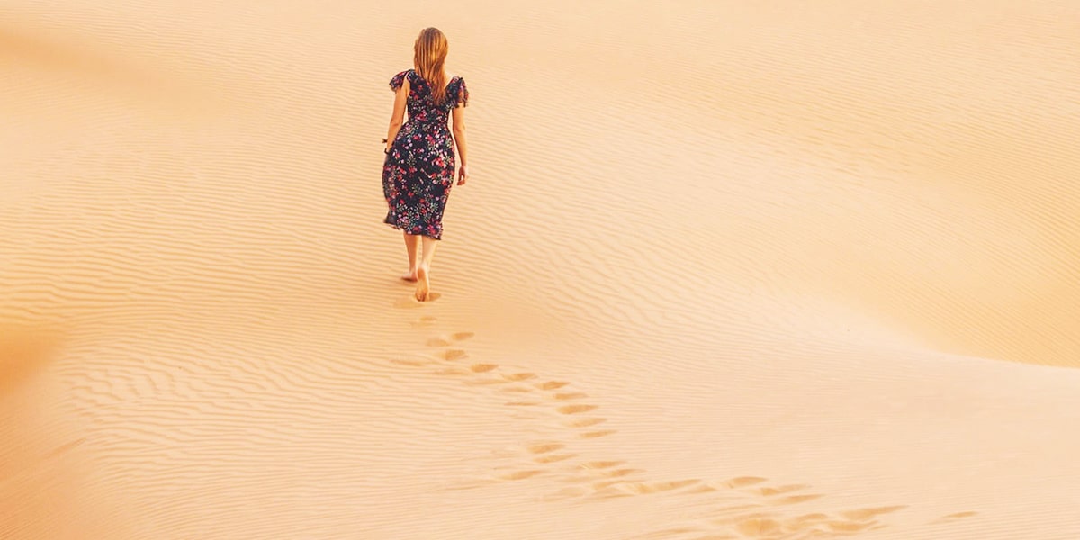 Woman walking in sand leaving behind footprints