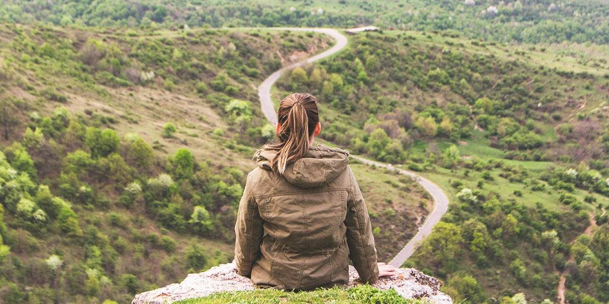 woman sitting on a rock overlooking a valley during her journey