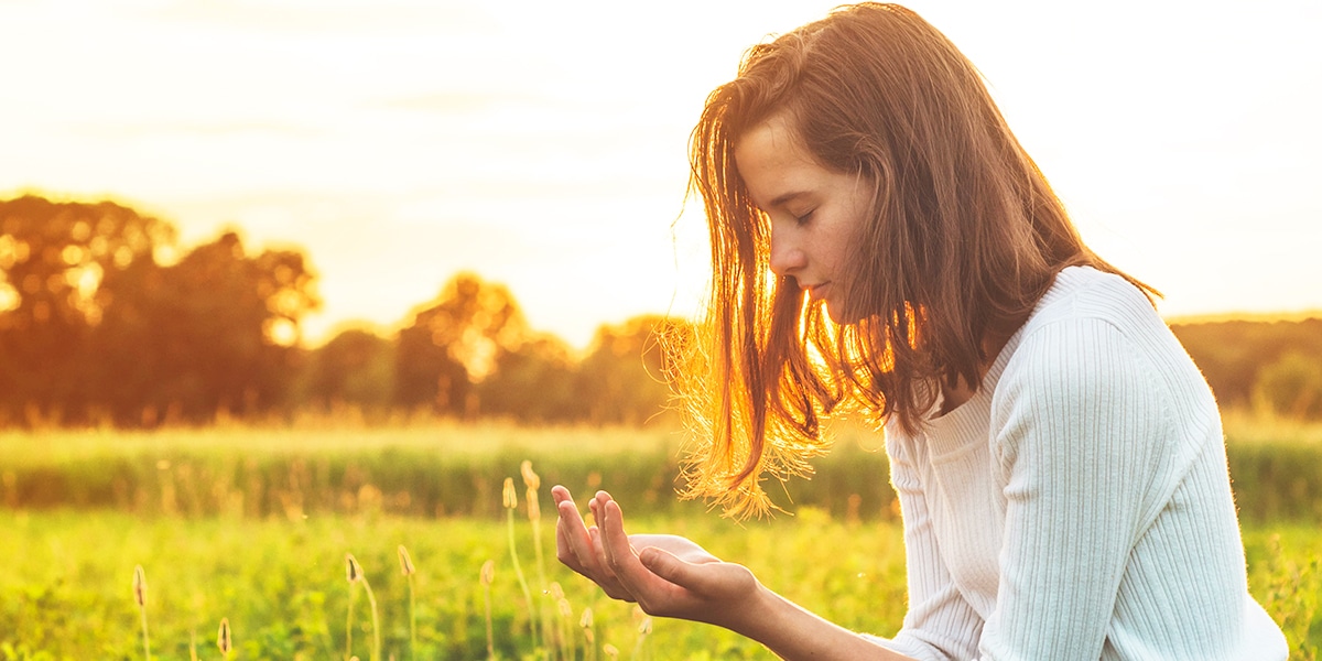 woman praying, receiving peace and grace, surrounded by sunlight and warmth.