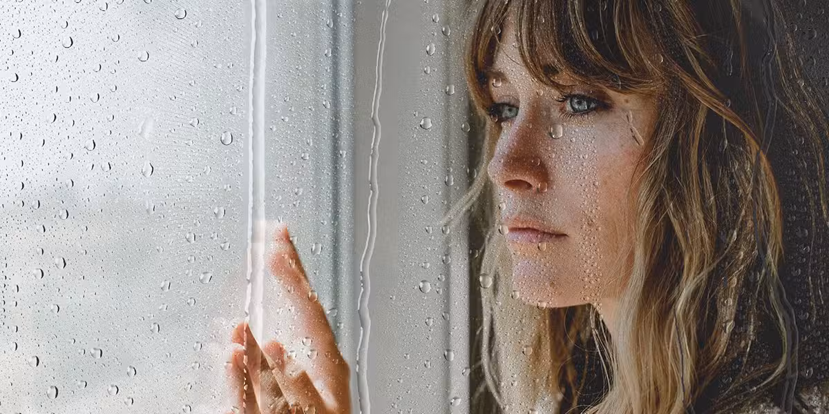 sad woman behind a window with water drops.