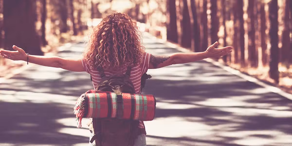 woman walking along a road carrying only a small backpack with a blanket